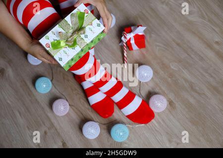 Woman in Christmas knee socks open the gift box sitting on a floor, New Year celebration Stock Photo