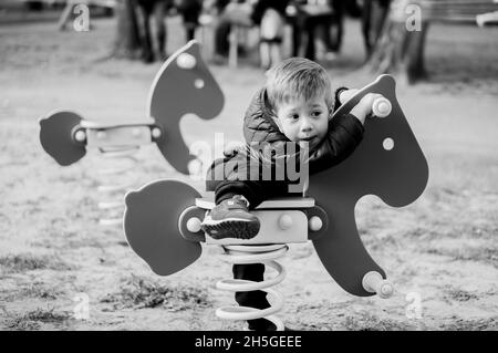 Grayscale shot of a cute Polish boy riding a horse on the playground Stock Photo