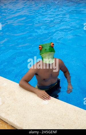 Vertical shot of a Caucasian male with a frog head in the swimming pool Stock Photo