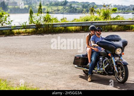 A couple sits on a motorcycle on a roadside turnoff on the Honoapiilani Hwy in North West Maui and posing for the camera; Maui, Hawaii, United States Stock Photo