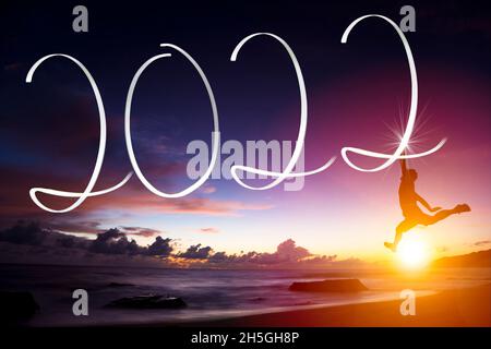 Man drawing 2022 by flashlight on the beach at sunrise.Happy new year 2022 concepts Stock Photo