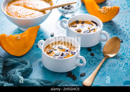 Homemade pumpkin soup with coconut milk, pumpkin oil and seeds on blue background Stock Photo