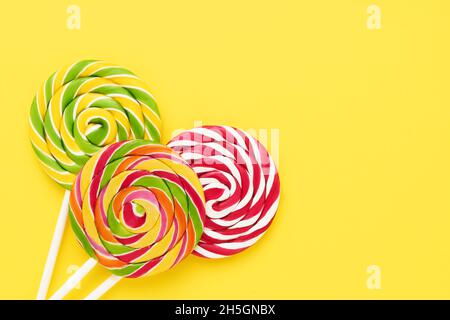Three colorful lollipops on a white stick on a bright yellow background. Top view, copy space for text Stock Photo
