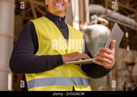 Joyful male worker using notebook at factory Stock Photo