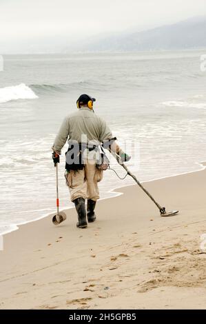 Man with a metal detector hunting for treasure at the beach Stock Photo