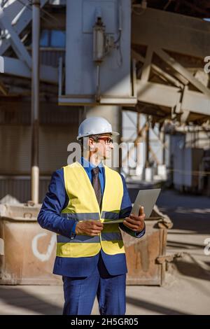 Joyful male engineer using laptop outdoors at factory Stock Photo