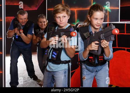 Teenage boy and sister aiming laser guns at other players during laser tag game Stock Photo