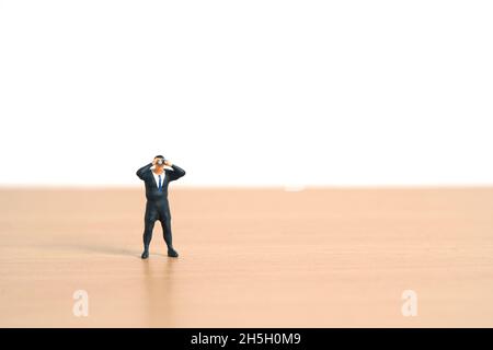 Businessmen standing using binoculars above wooden table. Miniature tiny people toys photography. Stock Photo