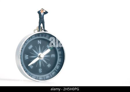Businessmen standing using binoculars above black compass. Miniature tiny people toys photography. isolated on white background. Stock Photo