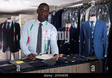 Smiling African-american man tailor taking order at counter in sewing workshop Stock Photo