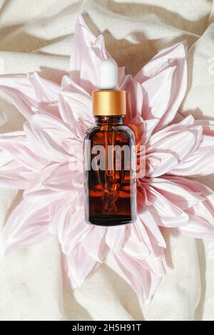 dark amber glass bottle with oil on flower and grey crumpled linen. Beauty concept, minimalism brand packaging mock up. Stock Photo