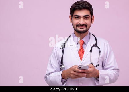 Young male doctor look at camera and smiling holding smartphone. Stock Photo