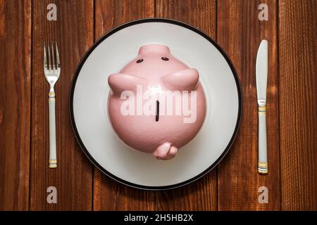 A pink piggy bank on dish. Savings consumer concept. Piggy bank on the plate with fork and knife. Financial concept Stock Photo