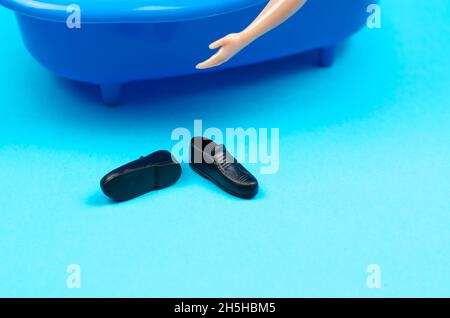 Men's shoes lie near the bath. Black shoes on a blue background. A man's hand reaches for the shoes Stock Photo