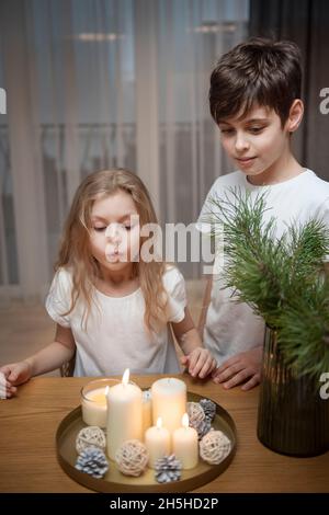 Cozy Christmas at home. Children - a boy and a girl blow out Christmas candles at home in the evening. Stock Photo