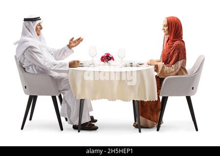 Arab man talking to a woman in a hijab seated at a restaurant table isolated on white background Stock Photo