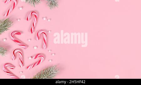 Banner with striped Christmas candy cane sweets, snowballs and for branches on pink background Stock Photo