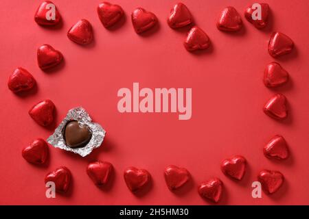 Romantic chocolate sweets as heart in red foil as frame on red background with copy space. Valentine's day greeting card. Love concept. Stock Photo