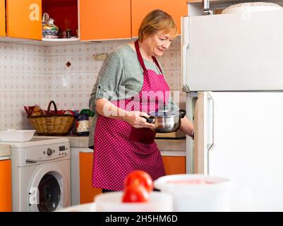 Aged housewife putting pan in fridge Stock Photo