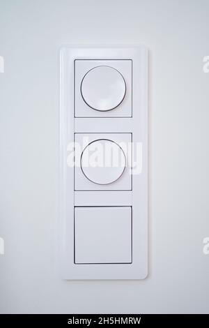 Triple light switch with dimmer on white wall Stock Photo