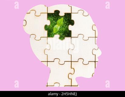 Woman's head profile shaped jigsaw puzzle with a green sprout visible through the missing piece on a pink background. The concept of developing a gree Stock Photo