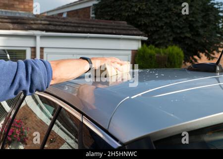 close up of mans hand holding a sponge, hand washing a silver car roof outside a house on a sunny day Stock Photo