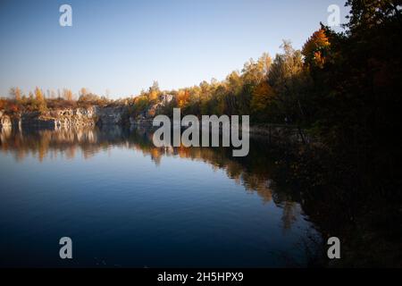 Rock cliffs with colorful autumn trees atop reflecting in calm water | Artificial water reservoir, former limestone quarry in Krakow, Poland Stock Photo