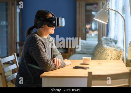 Woman in knitted sweater using vr virtual reality headset at home living room. For work or entertainment Stock Photo