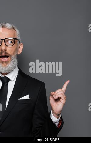 cropped view of surprised middle aged businessman in glasses and suit pointing with finger on grey Stock Photo