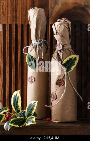 Homemade fruit wine in the bottles decorated with grunge paper, wax seal and green leaves of holly as small present for Christmas. Kitchen gift ideas Stock Photo
