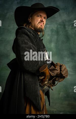 Cropped portrait of brutal horrendous man, medeival pirate in hat isolated over dark background. Stock Photo