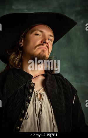 Cropped portrait of brutal man, medeival pirate in hat isolated over dark background. Stock Photo