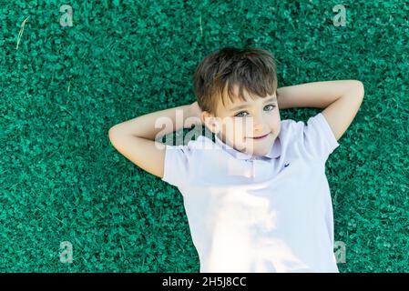 Smiling green-eyed boy lying on the grass with his hands on the back of his head Stock Photo