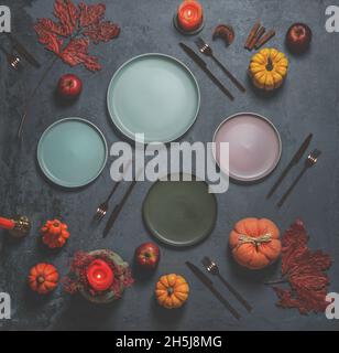 Autumn table settings with various empty plates on dark concrete kitchen background with cutlery, pumpkins, autumn leaves and candles. Preparing seaso Stock Photo
