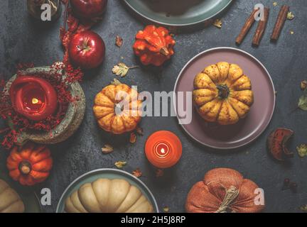 Various colorful pumpkins, candles, plates, cutlery and decoration on dark concrete kitchen table. Rustic autumn still life with seasonal vegetables. Stock Photo