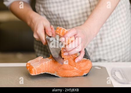 Removing fish bones. Woman in an apron prepares red fish fillets for cooking. Stock Photo