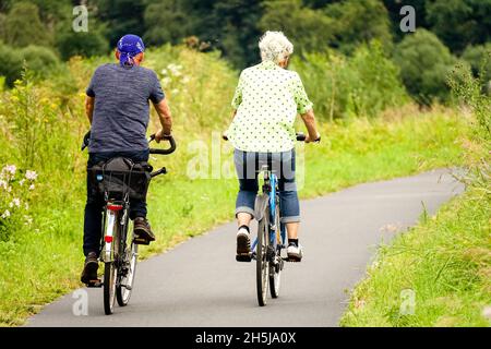 Senior couple ride on bike away on the cycle route, bicycle path along Elbe river Germany Saxony nature trail Stock Photo