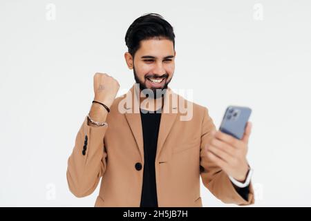 Portrait of a happy satisfied man looking at mobile phone and shouting isolated over white background Stock Photo