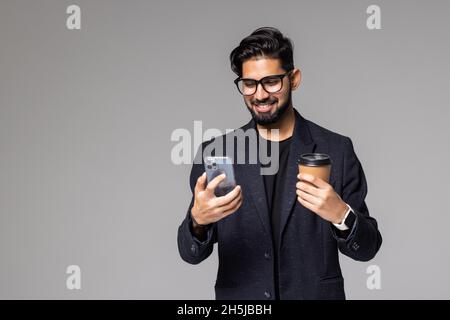 Handsome india man with backpack carrying cup of take away coffee and talking on phone when standing in office building Stock Photo
