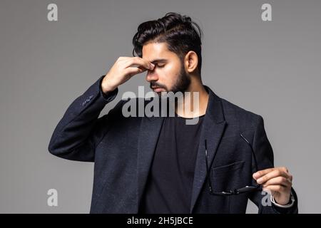 Young man covering face with hand and keeping eyes closed while standing against grey background Stock Photo
