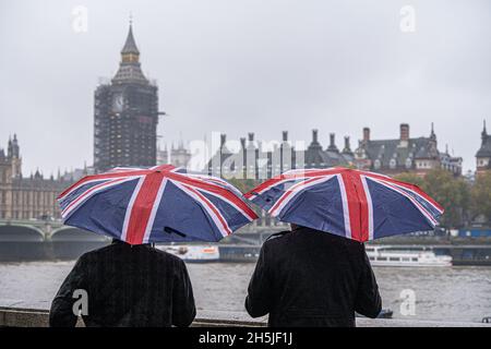 WESTMINSTER LONDON, UK. 10th Nov, 2021. Tourists with Union Jack umbrellas on Thames embankment on an overcast misty day with  outbreak of rain drizzle. Credit: amer ghazzal/Alamy Live News Stock Photo