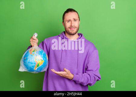 Photo of upset guy hold earth plastic bag think seriously we need live in hazard wear pullover isolated over green color background Stock Photo