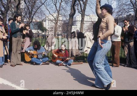 London 1982. A street view of a couple dancing to the music of street musicians sitting on the pavement with a park in the background. Credit Roland Palm. Stock Photo