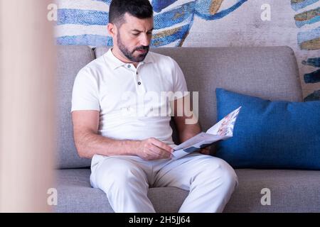 Attractive young man on the sofa in the hotel room flipping through a magazine. Stock Photo