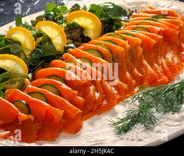 White Platter plate dish seafood smoked salmon slices fillet with lemon wedges fresh dill cucumber salad watercress Stock Photo