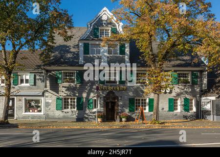 Germany, Haan, Bergisches Land, Niederbergisches Land, Niederberg, Rhineland, North Rhine-Westphalia, NRW, Becherhus in the Kaiserstrasse, half-timbered house with slate facade, green shutters, Bergisches Baroque, gastronomy, restaurant, autumnal trees, autumn colouring, fall foliage Stock Photo