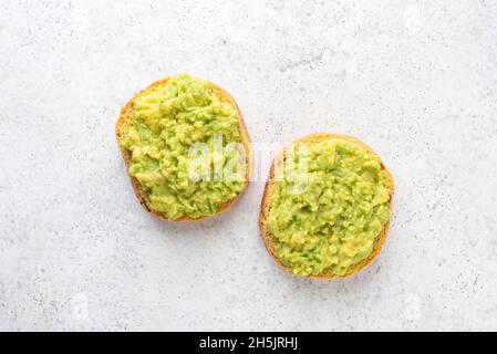 Mashed avocado on a round bun cut in halves. Healthy vegan avocado toast isolated on grey concrete background, table top view, copy space for text or Stock Photo