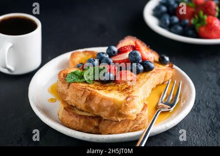 French toast with berries and syrup, black background, served with cup of espresso coffee Stock Photo