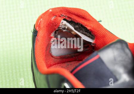 A ripped backdrop in sporty multicolored sneakers. Poor quality shoes, close-up, damaged Stock Photo