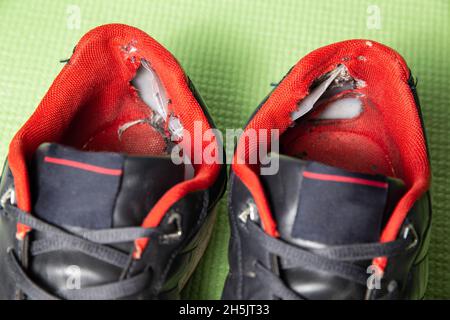 A ripped backdrop in sporty multicolored sneakers. Poor quality shoes, close-up, damaged Stock Photo